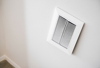 A white air vent mounted on a wall in a room.