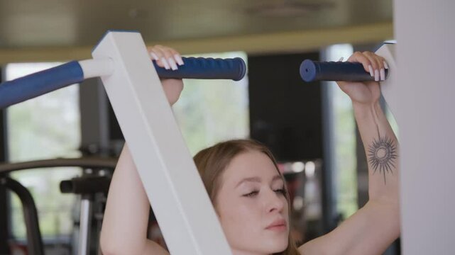 A young sportswoman does pull-ups on a machine in a gym. Concept of sport and healthy lifestyle, close-up