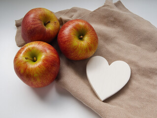 Fresh red apples with white wooden heart on beige cloth napkin, minimalist kitchen decor for healthy eating, Valentine's gifts, rustic home styling with natural light and organic textures. 