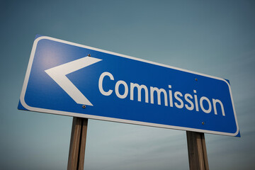 Blue road sign with white arrow pointing left and word "Commission" signifying direction or choice related to a commission