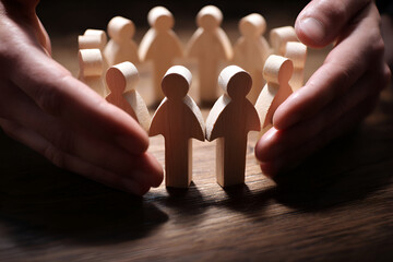 Hands gently cradling a circle of wooden figures, symbolizing protection