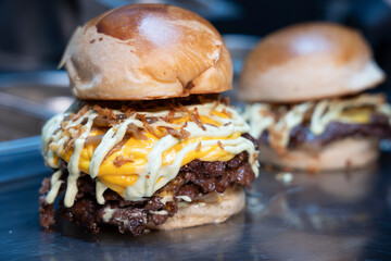 Freshly made double smash burgers with melted cheddar, grilled onions, and sauce on a shiny countertop..