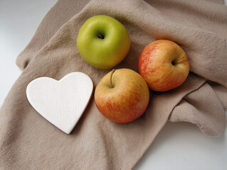 Fresh red apples with white wooden heart on beige cloth napkin, minimalist kitchen decor for healthy eating, Valentine's gifts, rustic home styling with natural light and organic textures. 