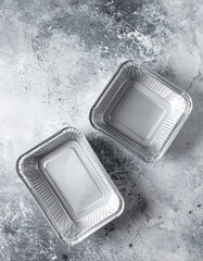 Two shiny silver foil containers, one slightly larger than the other, reflecting light beautifully, perfect for takeout or food storage.