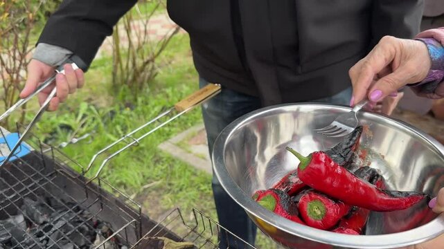Vegetables on the fire. Men's hands put grilled ramiro peppers into a bowl.