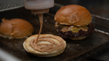 Chef adds special sauce to a burger bun during smash burger preparation