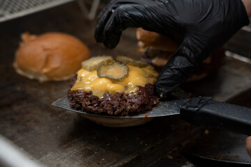 Chef adds pickles on melted cheese for smash burger assembly