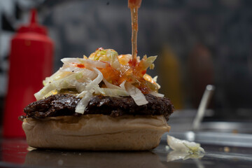 Chef adds hot sauce on a fresh smash burger with shredded lettuce