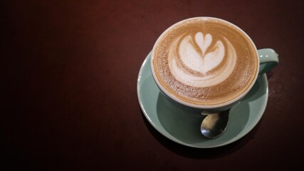 close up of a flat white coffee with a floral coffee art in a blue cup on a dark brown background with copy space