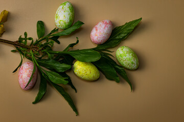 Colorful painted Easter eggs arranged with green leaves on a beige background. A simple and festive spring still life.