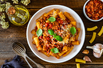 Rigatoni con ragù alla bolognese - noodles with bolognese sauce and grated parmesan cheese served in bowl on wooden table	
