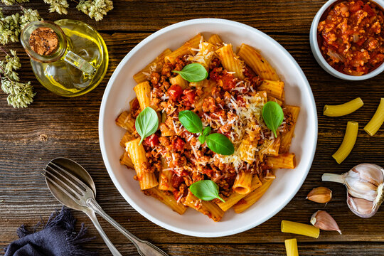 Rigatoni con rag&ugrave; alla bolognese - noodles with bolognese sauce and grated parmesan cheese served in bowl on wooden table	