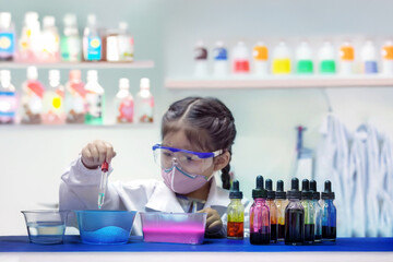wearing safety goggles and a mask, carefully uses a dropper to add liquid to colorful substances in...