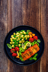 Seared salmon steak with gnocchi, green peas and tomatoes on wooden table	