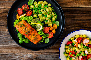 Seared salmon steak with gnocchi, green peas and tomatoes on wooden table	