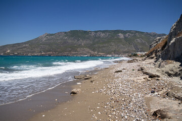 The beach of Loutraki stretches along the coast with sunbeds and clear blue waters, capturing the warmth and beauty of a Greek seaside summer.