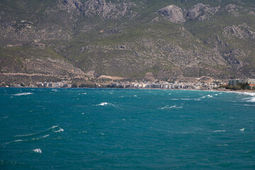 Obraz premium Crystal-clear blue waters near Loutraki sparkle under the sun, with a scenic mountain rising in the distance. A peaceful and inviting Mediterranean view ideal for travel and nature themes.