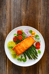 Fried salmon steak with green asparagus, cherry tomatoes and lime on wooden table