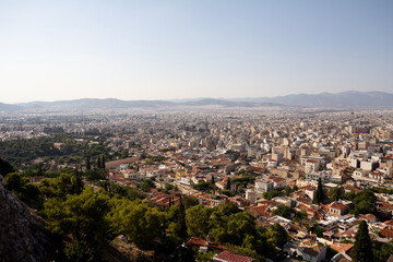 A panoramic view of Athens, Greece, seen from above. The city stretches out with a mix of historic and modern buildings, surrounded by hills under an open sky.