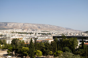 Obraz premium A panoramic view of Athens, Greece, seen from above. The city stretches out with a mix of historic and modern buildings, surrounded by hills under an open sky.