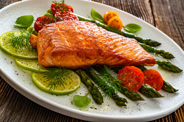 Fried salmon steak with green asparagus, cherry tomatoes and lime on wooden table