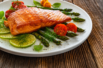 Fried salmon steak with green asparagus, cherry tomatoes and lime on wooden table