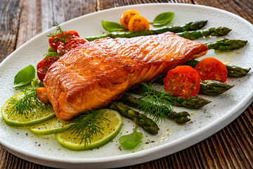 Fried salmon steak with green asparagus, cherry tomatoes and lime on wooden table