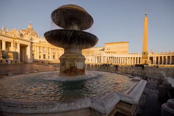 A majestic fountain in St Peters Square with Vatican architecture glowing under the sunset light....