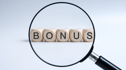Wooden cubes spelling BONUS viewed through magnifying glass, showcasing concept of reward, achievement, or financial gain