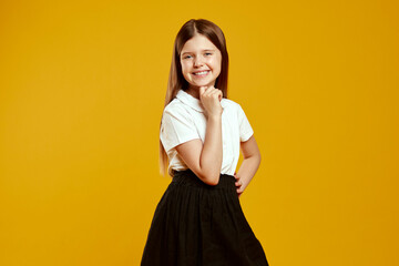 Smiling child in school attire poses joyfully, exuding confidence and happiness on a bright yellow backdrop. Ideal for educational materials and advertising campaigns.