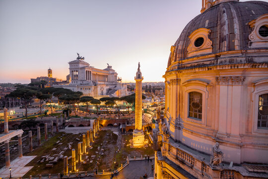 Scenic view of a historic dome and ancient Roman ruins glowing in the sunset light. The iconic Altare della Patria rises in the background above Romes evening skyline