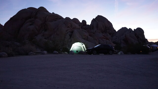 Glowing camping tent in the night with silhouette of large boulders in background