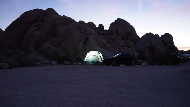 Glowing camping tent in the night with silhouette of large boulders in background