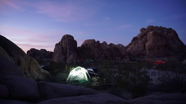 Glowing camping tent under a dusk sky with round boulders in background