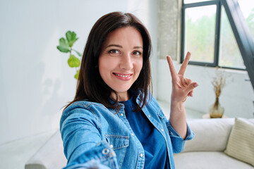 Selfie portrait happy beautiful woman making gesture victory success in home
