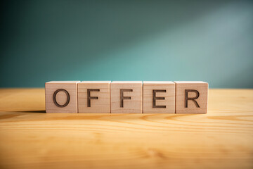 Wooden cubes spelling "OFFER" on light wood table against teal background, showcasing business proposal or marketing concept