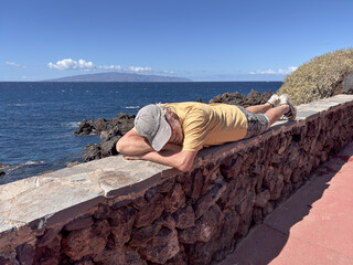 Senior man lying down along the seacoast enjoying relaxed moments in a sunny day. Horizon over...