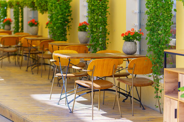 Cozy outdoor cafe with wooden tables and red flowers. Cozy atmosphere of public catering in the restaurant.