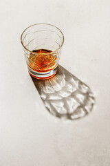 Transparent alcohol Glass with shadow at sunlight on beige concrete table, top view minimal style, aesthetic photo shiny glass sparkling at natural light, summer strong drink, still life,