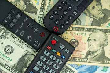 The concept of rising subscription prices. A few remote controls (TV, soundbar), USD, dollars (a...