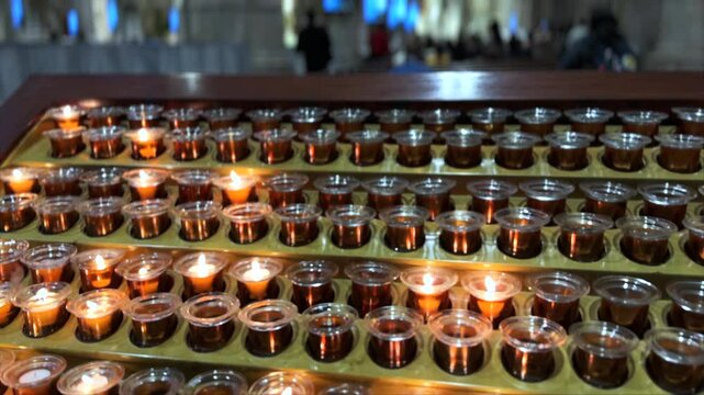 Rows of burning prayer candles in glass holders inside a cathedral, spiritual atmosphere and religious devotion concept.
