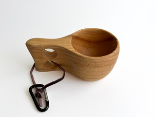 Side view of wooden Kuksa cup with a leather strap and carabiner.  Traditional Nordic style mug for outdoor adventures and camping.   Handcrafted wooden drinking vessel on a white background.