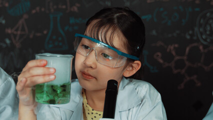 Young girl holding green chemical solution and inspect carefully while sitting in front of...