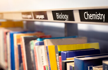 Books stacked on shelf under science categories of Biology and Chemistry. Non-fiction library or...