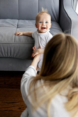 Mother and baby at home. Mom helping Child take first steps, emotional and heartwarming moment of early childhood development, parenting support, cozy indoor with natural light