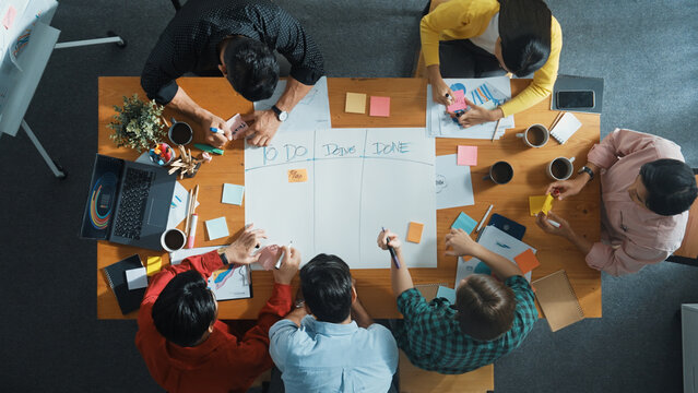 Top down aerial view of business team making scrum task board at meeting room. Group of people writing at paper and sticky notes for making kanban board to manage work flow. Top view. Convocation.