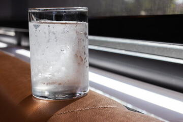 A cold glass of water with condensation sits on a brown surface by the window, catching natural...