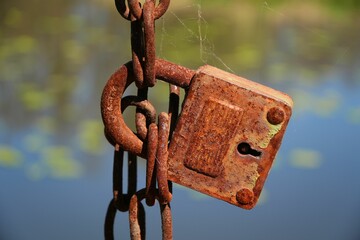 A rusty padlock on a rusty chain over the water.
