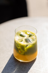 Glass of iced matcha latte on a sunlit table casting a long shadow. Bright and minimalistic composition. Refreshing healthy drink with vibrant green color, top view.