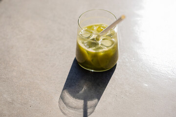 Glass of iced matcha latte on a sunlit table casting a long shadow. Bright and minimalistic composition. Refreshing healthy drink with vibrant green color, top view.